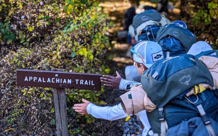 a group of students wearing backpacks pat an Appalachian trail sign on a trip with outward bound